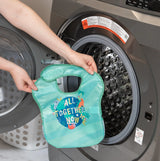 Placing a turquoise Bumkins SuperBib®: All Together Now into a washer, known for its durable and waterproof fabric.