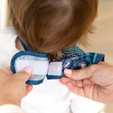 An adult fastens the SuperBib® from Bumkins, part of the All Together Now 3 Pack, around a childs neck using Velcro.