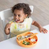 A toddler in a Bumkins SuperBib® from the Happy Campers pack enjoys rice, broccoli, and fruit from a sectioned plate for easy cleaning.