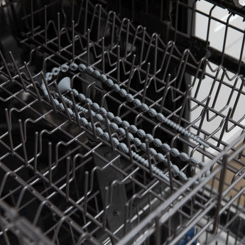 A Bumkins Silicone Accessory Tether 2-Pack in gray lies neatly in an empty dishwasher rack.