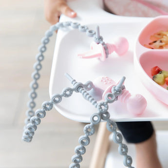 Bumkins high chair tray includes a pink divided plate with silicone tethers and dangling pink pacifiers.