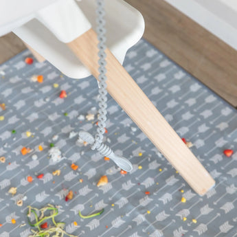 High chair on a mat with food debris, featuring Bumkins Silicone Accessory Tether 2-Pack: Gray for sensory play.