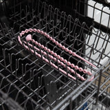 A Bumkins Silicone Accessory Tether in pink for teething babies rests on the top rack of an open dishwasher.