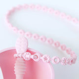 Close-up of a pink Silicone Accessory Tether by Bumkins, featuring textured beads and shaped like a spoon for teething babies.