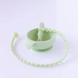 A mint-green baby feeding set by Bumkins, includes a suction bowl, spoon, and beaded pacifier clip in food-grade silicone.