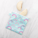 A Bumkins Reusable Snack Bag from the Large 2-Pack: Rainbows & Unicorns, rests on a marble surface. Made of waterproof fabric, it easily holds two crustless sandwich halves and is machine washable for convenience.