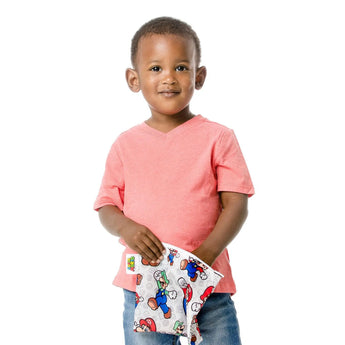 A young boy in a coral shirt and jeans holds a Bumkins Super Mario™ & Luigi reusable snack bag.