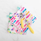 Bumkins reusable snack bags in Watercolor & Brush Strokes, with fork and spoon, shown on white marble.