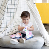 A toddler sits in a waterproof tent holding a colorful toy. The checkered tent has a durable zipper, and theres a yellow chair nearby.