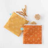 Bumkins Reusable Snack Bag, Large 2-Pack in Sunshine and Grounded patterns are on a white surface, filled with pretzels and stars.