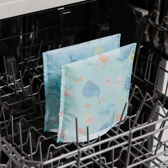 Two Bumkins reusable snack bags from the Ocean Life & Whale Tail collection sit open in an empty dishwasher for cleaning.