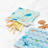 Bumkins Reusable Snack Bag, Large 2-Pack: Ocean Life & Whale Tail, one open with veggie sticks and one closed with pretzels on a white surface.