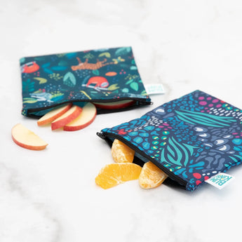 Two Bumkins reusable snack bags, Jungle & Animal Prints, hold apples and oranges with durable zipper closures on a white surface.