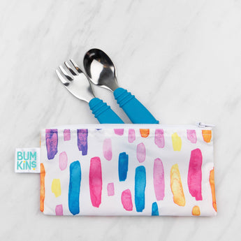 Colorful Bumkins pouch from the Reusable Snack Bag 2-Pack holds a fork & spoon with blue handles on a marble surface.