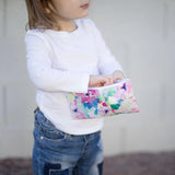 A child in a white shirt and jeans holds a Bumkins Watercolor Snack Bag against a plain background.