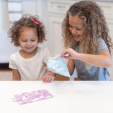 Two curly-haired girls smile as they play with Bumkins Reusable Snack Bags, Rainbows & Unicorns, at a white kitchen table.