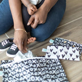 A parent and child sit with Bumkins XOXO & Hearts snack bags, while the child wears black shoes with pink laces.