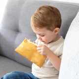 A child on a gray couch peers into a Bumkins Reusable Snack Bag, Small, Sunshine—a stylish pouch with white eye patterns.