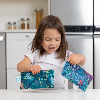 Young girl joyfully playing in kitchen with Bumkins Reusable Snack Bag, Small 2-Pack: Jungle & Animal Prints.