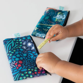 A child holds a snack near Bumkins waterproof, machine-washable Jungle & Animal Prints Reusable Snack Bag; another bag is in the background.