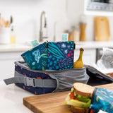 Bumkins Reusable Snack Bags in Jungle & Animal Prints sit by a sandwich and banana, highlighting eco-friendly charm on the counter.