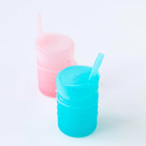 Two translucent Bumkins silicone straw cups, blue and pink, designed for independent drinking skills, on a white background.