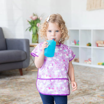 A child with curly hair in a unicorn shirt drinks from a blue Bumkins Silicone Straw Cup.