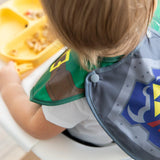 A child in a high chair wears Bumkins Caped SuperBib®: The Legend of Zelda™ Link, ready to eat with the easy-wipe bib for protection.