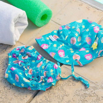 Bumkins Swim Set: Mermaids (UPF 50+) and a white towel beside a green pool noodle on tiled poolside floor.