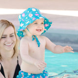 A baby beams in the pool wearing Bumkins Swim Set: Mermaids, while an adult nearby shares a smile.