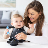 A woman feeds her baby with a Bumkins Silicone Dipping Spoon (Mickey Mouse black) while the baby wears a Mickey Mouse bib.