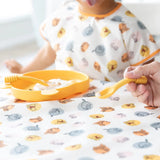 A child enjoys yogurt from Bumkins Winnie the Pooh Silicone Dipping Spoons on a tablecloth in a patterned bib.