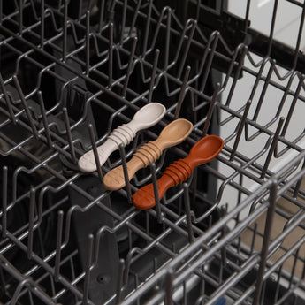 The Bumkins Silicone Dipping Spoons 3 Pack in Rocky Road is neatly placed on the top rack of an open dishwasher.