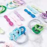 Bumkins Silicone Teething Charms: Blue, arranged on a white marble surface.