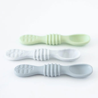 Three pastel silicone dipping spoons from the Bumkins Silicone Dipping Spoons 3 Pack: Taffy are arranged on a white surface. The set includes green, white, and blue spoons with textured grips and rounded bowls, ideal for teaching infants self-feeding skills.