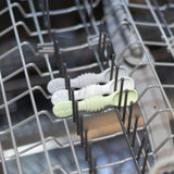 Two Bumkins silicone dipping spoons from the 3-pack Taffy set rest on the top rack of an open dishwasher among metal prongs.