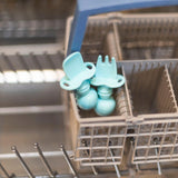 Two Bumkins Silicone Chewtensils®, blue with sensory bumps, sit in the dishwashers utensil basket.