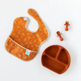 Orange baby bib, silicone plate & Clay Chewtensils® set by Bumkins—all food-safe silicone on a white background.