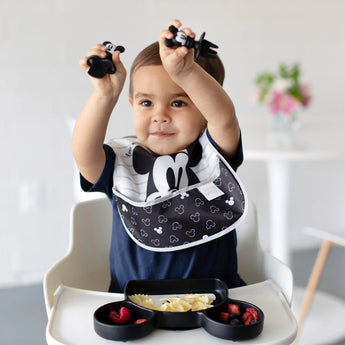 Toddler in a high chair with Bumkins Silicone Chewtensils®: Mickey Mouse, enjoying pasta & raspberries—ideal for baby-led weaning.