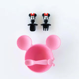 The Bumkins Silicone Chewtensils®: Minnie Mouse set includes a pink, mouse-shaped plate with attached spoon and fork. Above are black utensils featuring mouse ear handles with red bows, ideal for baby-led weaning, all displayed against a white background.