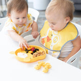 Two toddlers enjoy fruit and cereal from a yellow plate, using Bumkins Silicone Chewtensils®: Winnie The Pooh for their weaning.