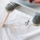 Toddler feet in shoes on a chair, crumbs from baby-led weaning, Silicone Chewtensils®: Gray by Bumkins and a blue pacifier nearby.