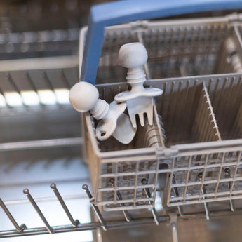 Two Bumkins Silicone Chewtensils® in gray with round handles sit in a dishwashers cutlery basket.