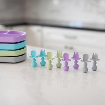 Bumkins Silicone Chewtensils® in Lavender are neatly arranged on a white kitchen counter, ideal for baby-led weaning.