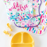 Bright Bumkins bibs with floral and striped designs, plus Silicone Chewtensils® in Pineapple for a fun, food-safe meal experience.