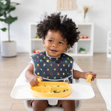 A toddler in a bright room sits in a high chair, embracing baby-led weaning with Bumkins Silicone Chewtensils®: Pineapple.