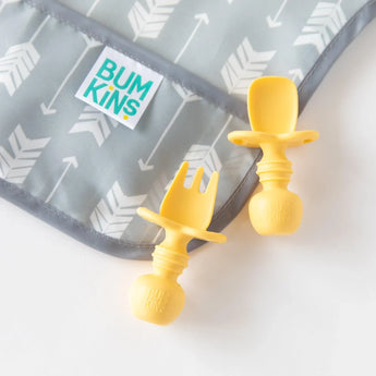 Yellow Bumkins Silicone Chewtensils®: Pineapple with sensory bumps, next to a gray patterned bib with arrow designs.