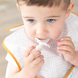 A toddler with a bib chews on a Bumkins Silicone Chewtensils®: Sand teether, ice cream-shaped and made from 100% food-safe silicone.