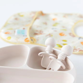 The Bumkins baby feeding set includes a beige divided plate, Silicone Chewtensils® in Sand, and a colorful bib for baby-led weaning.