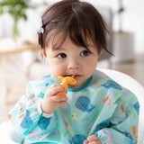 A toddler uses Bumkins Silicone Chewtensils®: Tangerine, a teething toy made of 100% food-safe silicone, while wearing a sea creature bib.